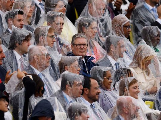 Britain's Prime Minister Keir Starmer (C) looks on as other attendees around him wear rain covers to protect themselves from the rain during the opening ceremony of the Paris 2024 Olympic Games in Paris on July 26, 2024.