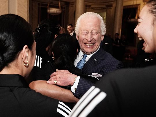 Britain's King Charles III reacts as he is hugged by members of New Zealand's Black Ferns rugby union team