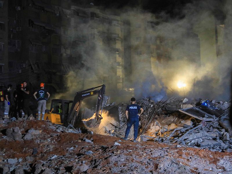 People and first responders stand on the rubble of a builiding destroyed