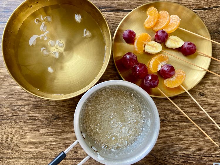 Once the sugar mixture is ready, dip the fruit skewers into it and immediately place them in ice-cold water.